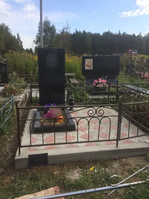 Два памятника на семейном участке со светлой плиткой и металлической оградой