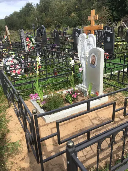 Светлый памятник с резным ангелом внутри строгой ограды