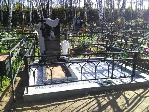 Черная стела с резной драпировкой и белой фигурой у цветника