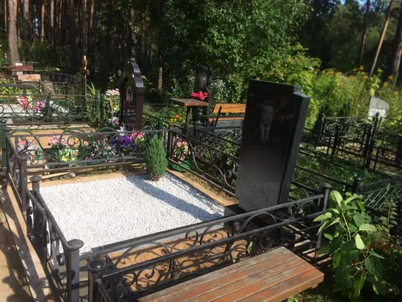 Участок с белой отсыпкой и деревянной скамьей за ажурной оградой