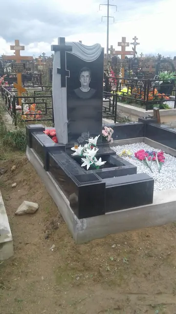 Памятник с резным крестом и белой крошкой внутри цоколя