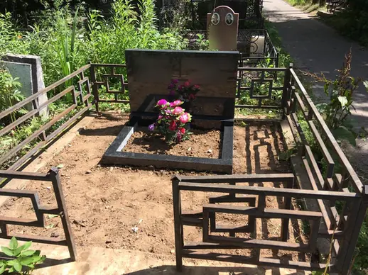 Горизонтальный памятник с цветами внутри коричневой ограды