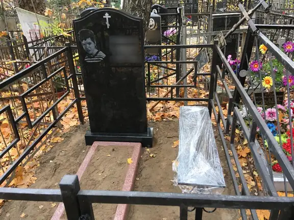 Черная арочная стела с портретом на участке в строгой ограде