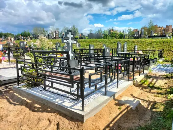 Серый крест на белой крошке внутри геометрической ограды