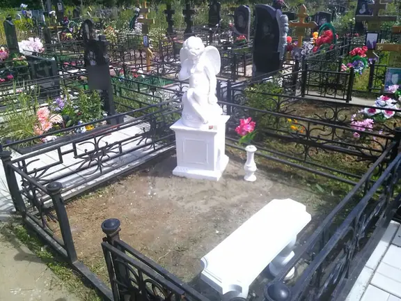 Белая скульптура ангела на постаменте в кованой ограде