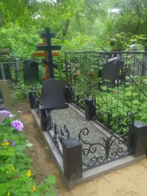 Памятник с высоким православным крестом за ажурной оградой
